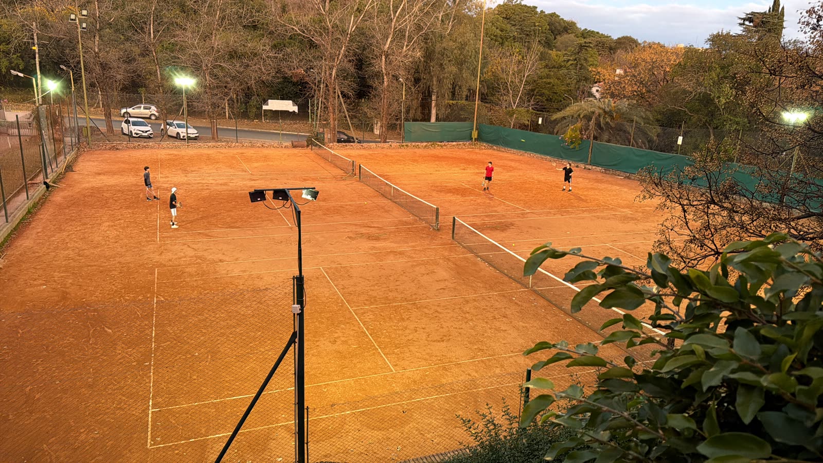 Canchas de polvo de ladrillo iluminadas al atardecer con jugadores
